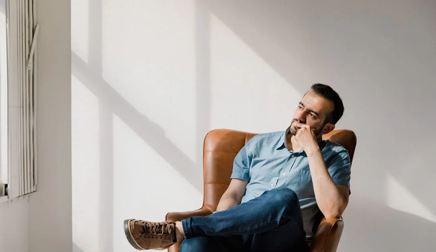 A person sitting thoughtfully in a leather armchair in a sunlit room