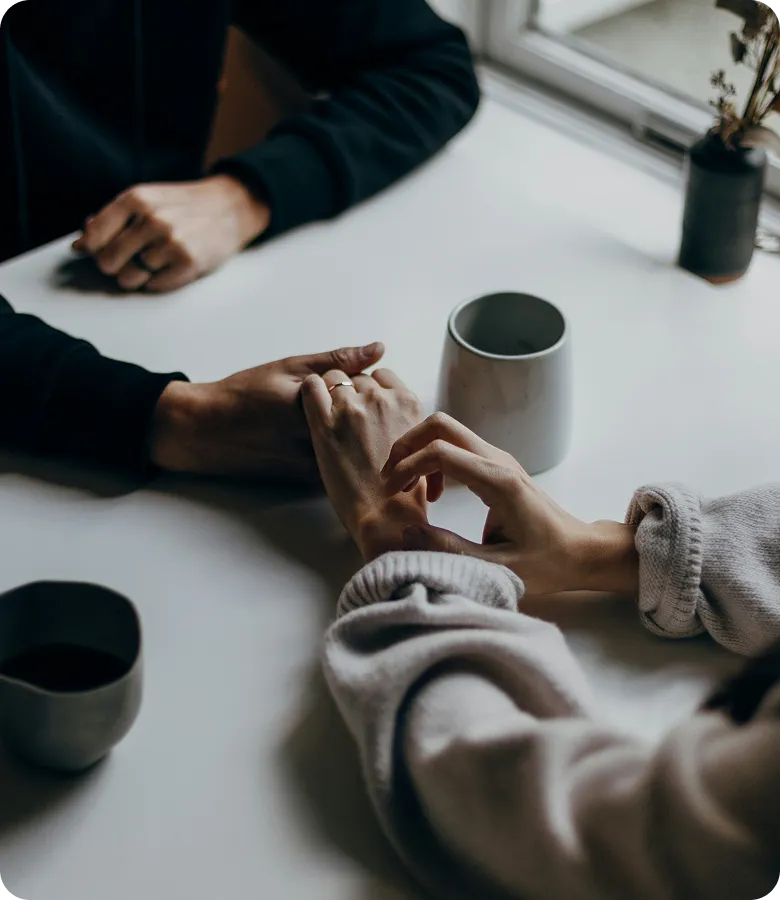 Two people holding hands across a table beside cups of coffee