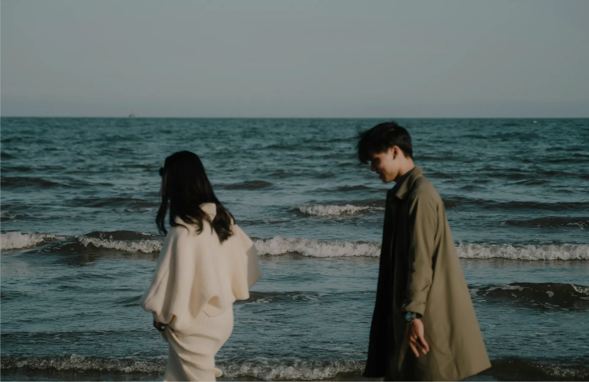 A couple walking apart along the shore at the water’s edge