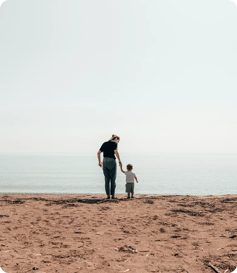 A mother walking hand in hand with her young child along the beach