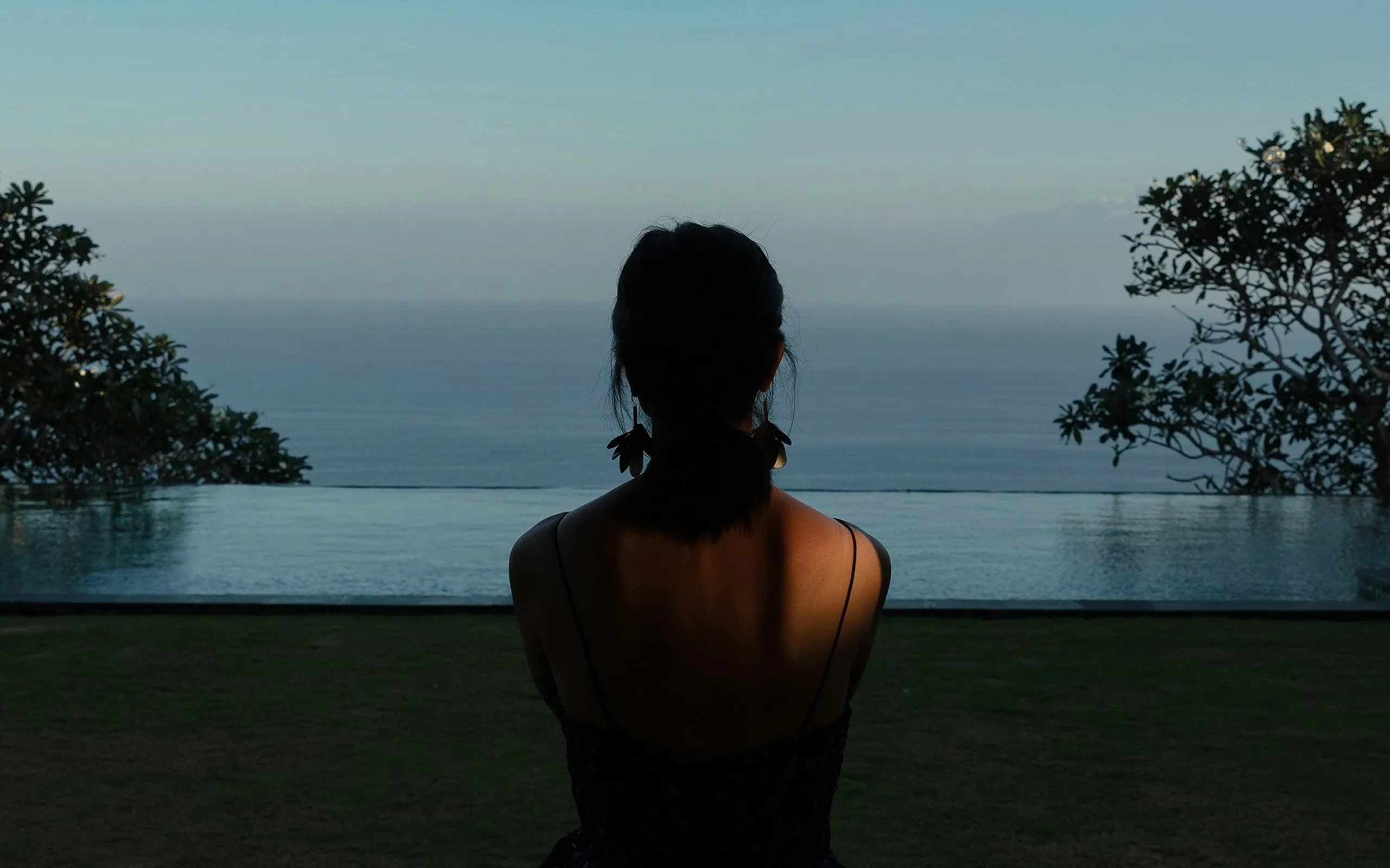 A woman sitting in front of an infinity pool overlooking the ocean in Bali