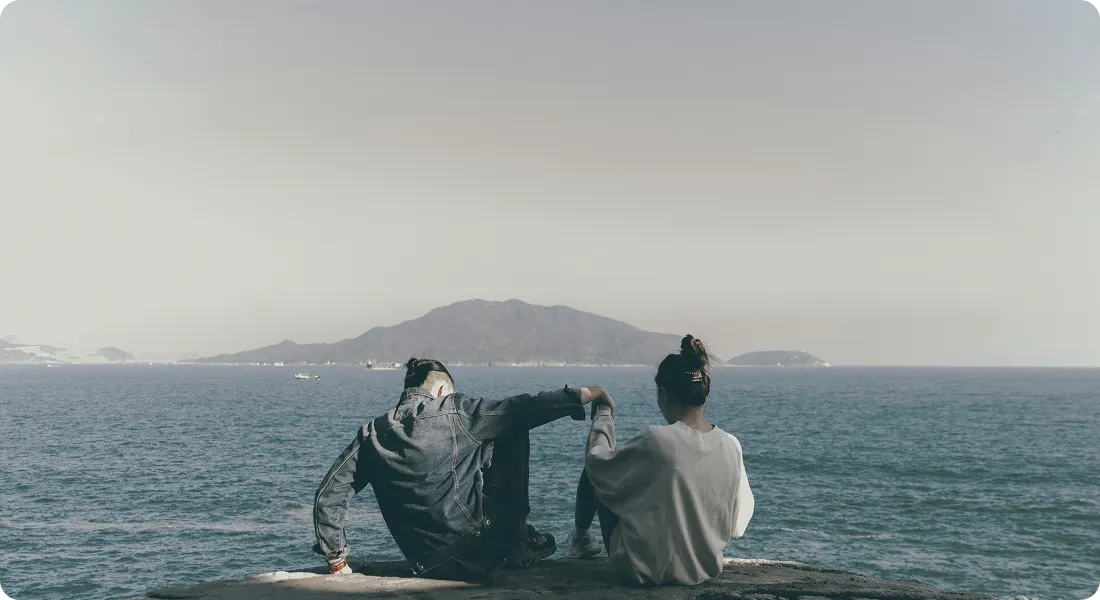 A couple sitting side by side on the rocks, looking out to sea